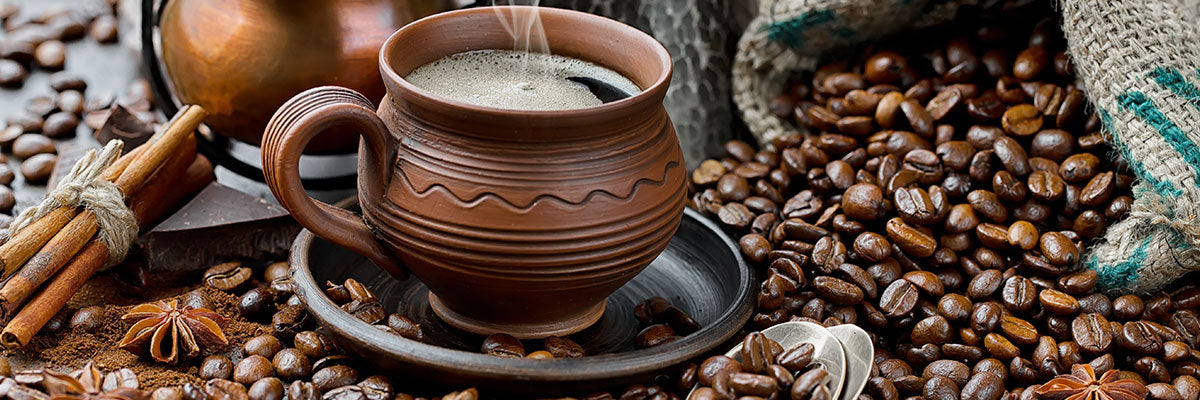 Coffee Beans spilling out of a burlap sack surrounding a clay colored coffee mug